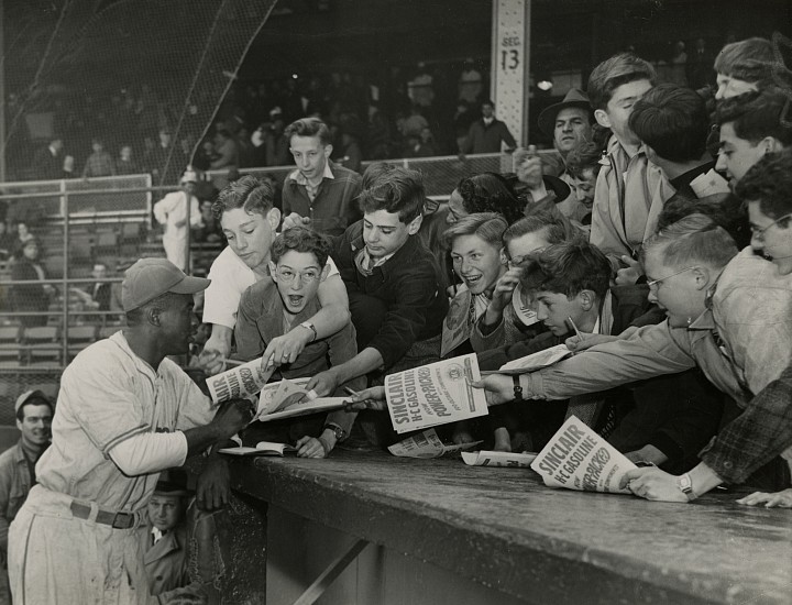 Unidentified photographer, Jackie Robinson stands surrounded by eager autograph seekers, c. April 22-24, 1947
Gelatin silver print, 6 1/2 x 8 1/2 in. (16.5 x 21.6 cm)
Annotated "Jackie Robinson" in pencil and "Baseball File" in red pencil with International News Photos stamp and headline "Young Fans Besiege Their Hero" affixed to print verso.
Illustrated: The Chicago Star, April 26, 1947, p. 20 with the caption: "Jackie Robinson, first Negro to crash the Jim Crow barriers of major league baseball, stands surrounded by eager autograph seekers. As first baseman for the Brooklyn Dodgers, Jackie has already begun to show the form that made him the most valuable player in the International League last season." 
8502