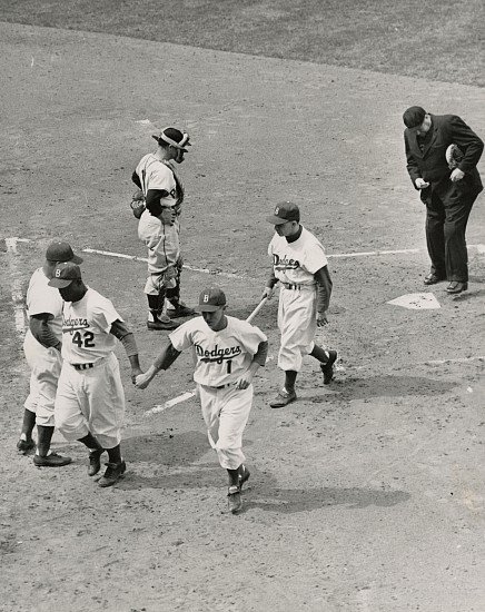 Barney Stein, Robinson and Reese hold hands, April 15, 1954
Gelatin silver print; printed later, 9 9/16 x 7 9/16 in. (24.3 x 19.2 cm)
Resin coated print. Photographer's stamps and address with typed caption taped to print verso.
Caption reads, "From Barney Stein/Here's an action shot one will seldom/ see in baseball as Jackie Robinson and/ Captain Pee Wee Reese hold hands on/ [after] crossing the plate on/ Jacki[e] Robinson'/ homer. Dodgers' bat boy Joey [sic; Charlie] Di Giovanna/ walks behind them as he carries Jackie's/ bat."
8504